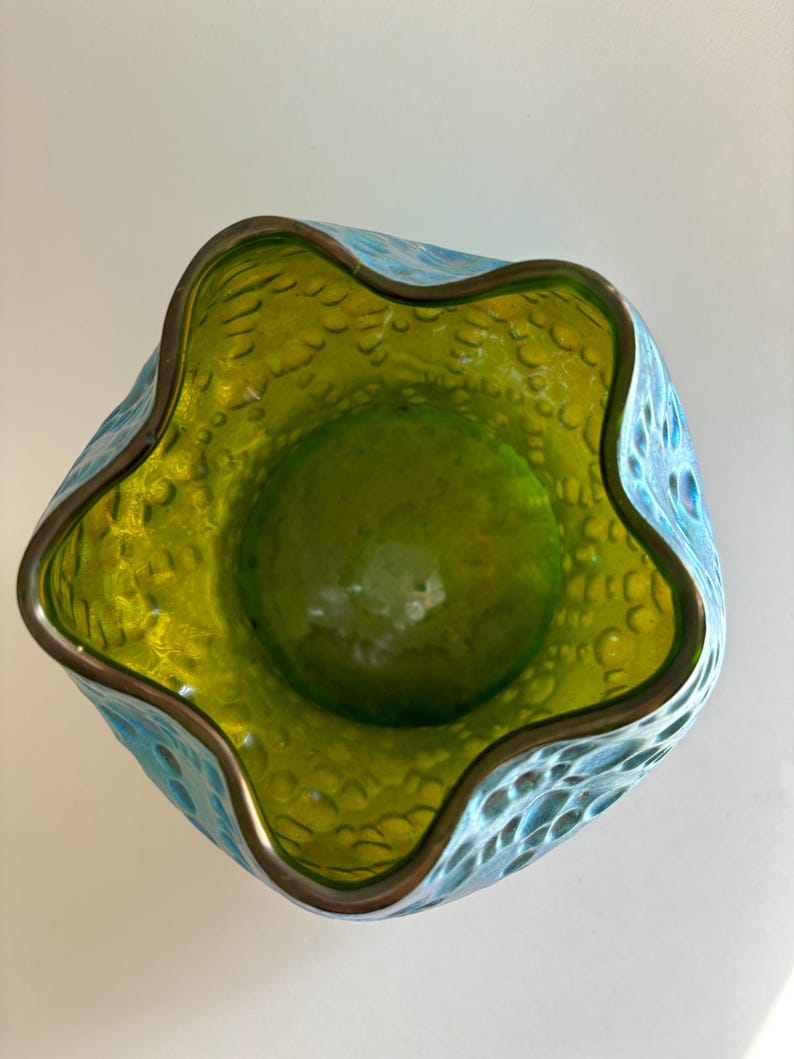 May include: A glass bowl with a wavy, five-pointed star-shaped rim. The interior is a vibrant lime green, while the exterior features a textured, bubbled surface in a bright turquoise blue. The rim is finished with a thin, metallic bronze edge.