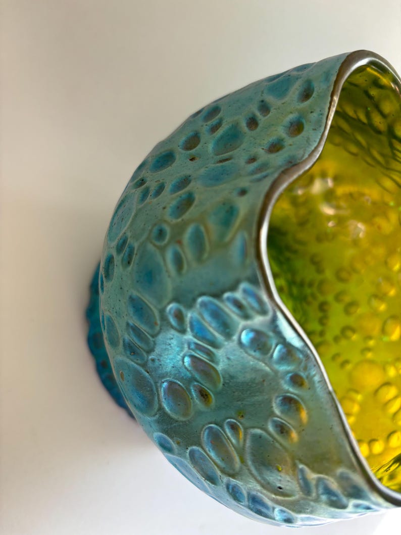 May include: A glass bowl featuring a textured exterior with a metallic turquoise finish and a smooth, vibrant lime green interior. The rim has an irregular, wavy shape, and the outer surface is covered in raised, circular, bubble-like indentations.