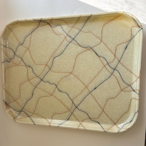 May include: A rectangular serving tray with rounded corners, featuring a cream-colored base with a translucent, textured appearance. The surface is decorated with a grid of thin, intersecting wavy lines in black and burnt orange colors.