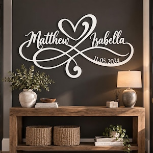 Op de afbeelding: Een wit wandbord met de namen Matthew en Isabella in cursief schrift, geïntegreerd met een oneindigheidssymbool en een hartvorm. De datum 11.05.2024 staat weergegeven in het rechtsonder gedeelte van het witte uitgesneden ontwerp.
