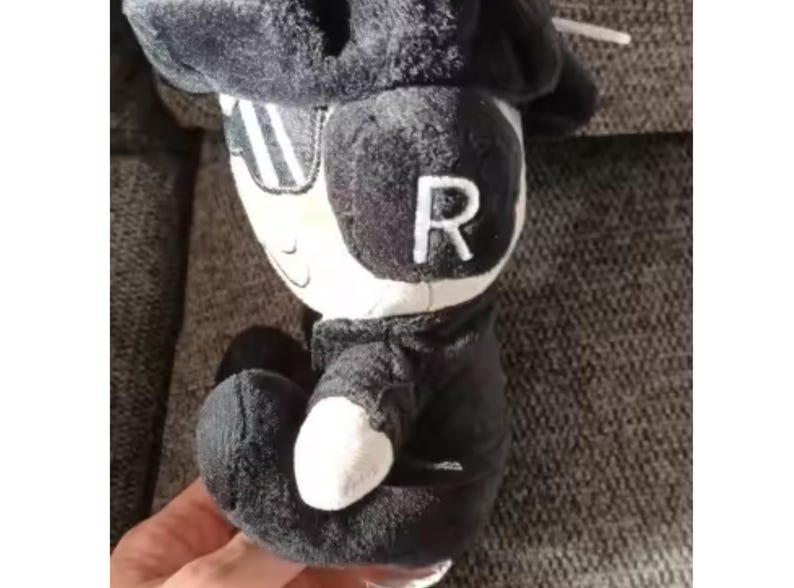 May include: A black and white plush toy of a character wearing a hat and sunglasses, with the letter "R" on its head. The toy has a white face and hands, and is dressed in a black outfit.