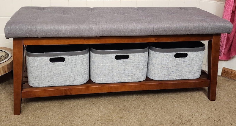 May include: A wooden storage bench with a gray upholstered top and three gray fabric storage bins. The bench has a dark brown frame and is suitable for a bedroom or entryway.