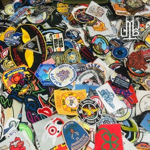 Puede incluir: Una colección de parches bordados con varios diseños y texto. Los parches incluyen logotipos, insignias y emblemas, con texto como "FORTIFIED", "POLICE" y "ENGINE 2". Los parches son de varios colores y formas, algunos con temas militares o relacionados con el servicio.