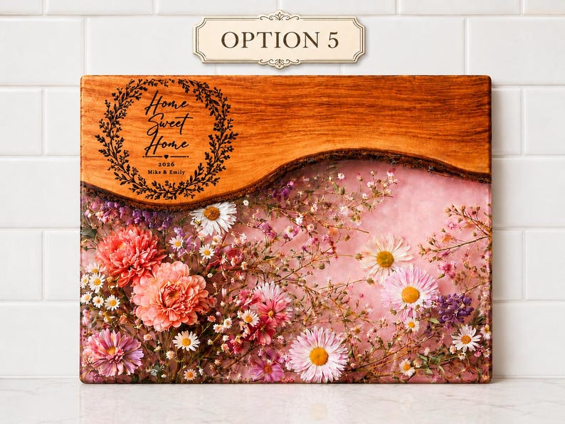 May include: Rectangular wooden cutting board with a live edge and a floral resin design. The top section is engraved with "Home Sweet Home" and the names "Mike & Emily" and the year 2026. The resin section is filled with pink and white flowers.