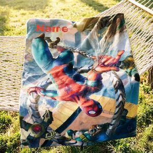 May include: A rectangular fleece blanket featuring a vibrant graphic of the superhero Spider-Man in a dynamic action pose against a city backdrop, with the word Name printed in red at the top left corner and mechanical tentacles visible below.