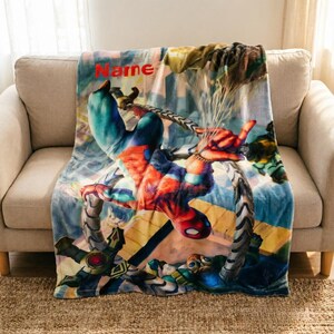 May include: A soft fleece throw blanket featuring a vibrant, full-color graphic of Spider-Man in a dynamic action pose with mechanical tentacles. The word Name is printed in bold red letters at the top left corner of the blanket design.
