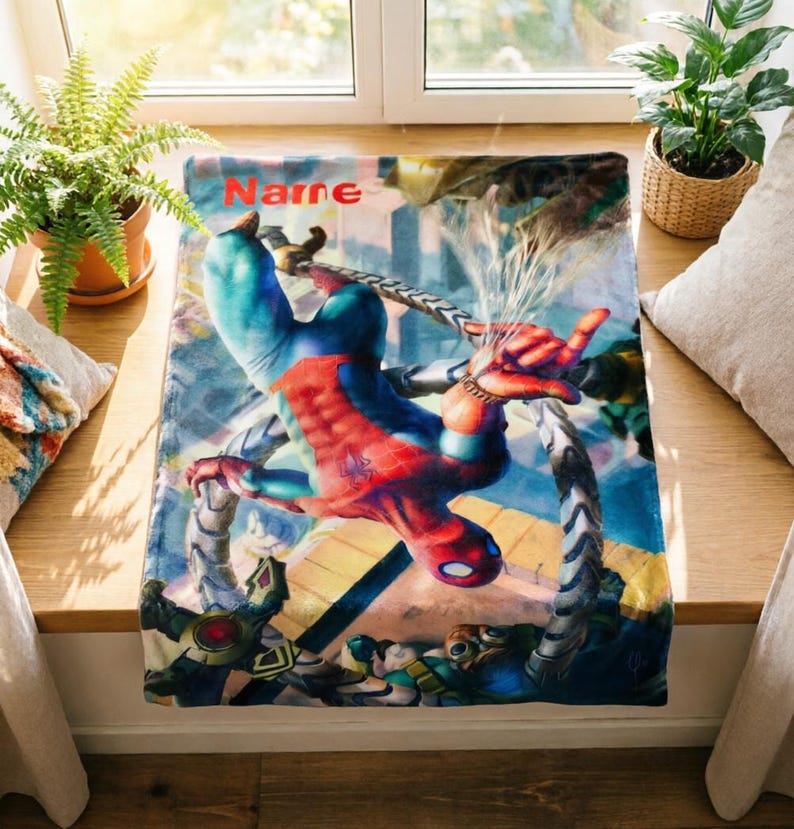 May include: A rectangular fleece blanket featuring a vibrant graphic of Spider-Man in a red and blue suit, suspended by mechanical tentacles. The word Name is printed in orange at the top. The design includes detailed action imagery of the character.