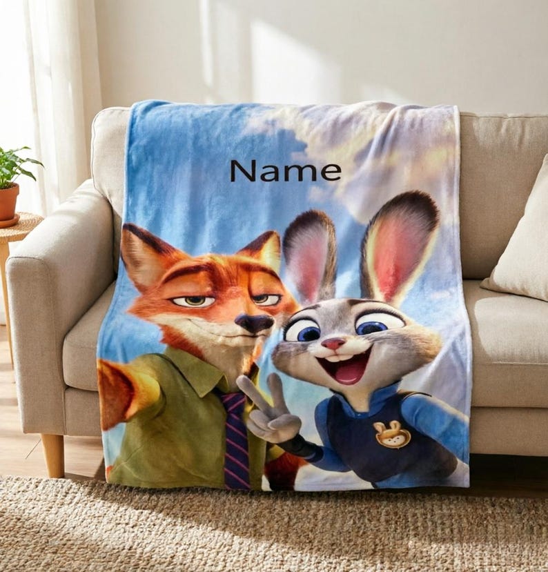 May include: A plush blanket featuring the animated characters Nick Wilde and Judy Hopps from Zootopia. The blanket has a blue sky background with the word "Name" printed on it. The characters are in full color, with Nick in a green shirt and Judy in a blue uniform.