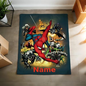 May include: A rectangular throw blanket featuring a vibrant graphic illustration of Spider-Man surrounded by various comic book villains including Venom, Carnage, and Rhino. The word Name is printed in bold orange letters at the bottom center.