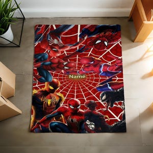 May include: A rectangular blanket featuring a vibrant red spiderweb pattern background with multiple illustrations of Spider-Man in various action poses and a black Venom character. The word Name is printed in the center of the design.