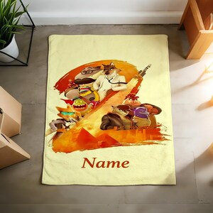 May include: A rectangular, light yellow bath towel featuring a colorful illustration of animated characters with a fiery background. The word "Name" is printed in a dark red script at the bottom of the towel.