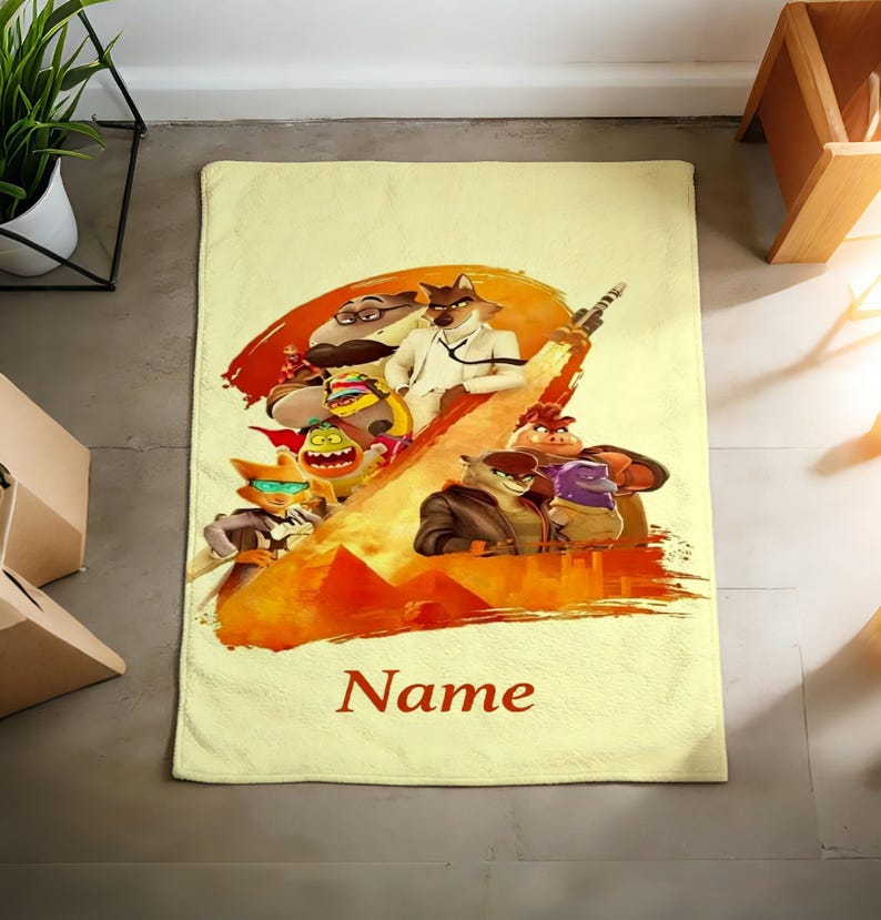 May include: A rectangular, light yellow bath towel featuring a colorful illustration of animated characters with a fiery background. The word "Name" is printed in a dark red script at the bottom of the towel.