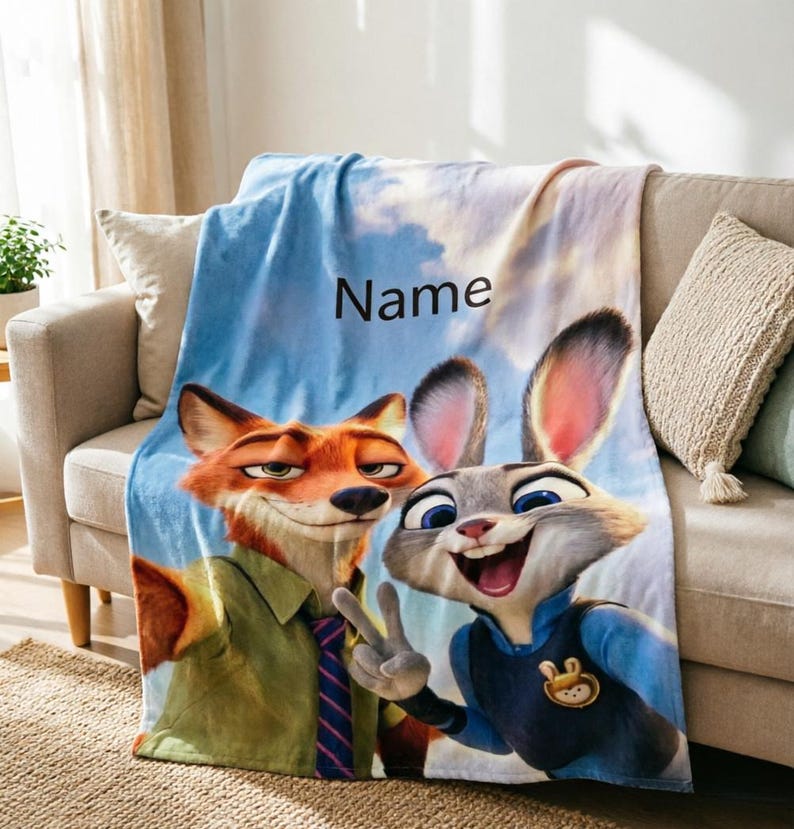 May include: A plush blanket featuring the animated characters Nick Wilde and Judy Hopps from Zootopia. The blanket has a blue sky background with the word "Name" printed on it. The characters are in a selfie pose.