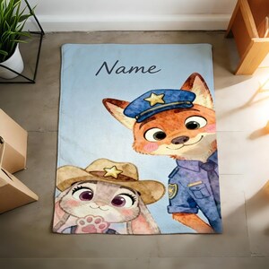 May include: A light blue blanket featuring cartoon characters of a fox in a police uniform and a bunny wearing a cowboy hat. The blanket has the word "Name" in cursive script.