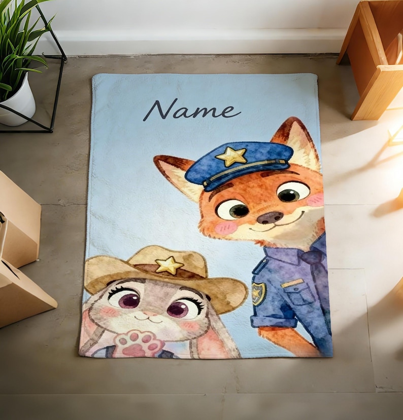 May include: A light blue blanket featuring cartoon characters of a fox in a police uniform and a bunny wearing a cowboy hat. The blanket has the word "Name" in cursive script.