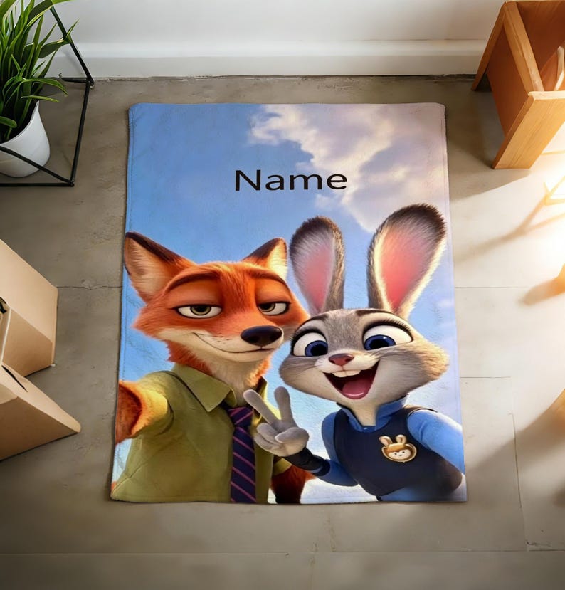 May include: A rectangular blanket featuring the characters Nick Wilde and Judy Hopps from Zootopia, set against a blue sky background. The blanket has the word "Name" printed on it. The fox is wearing a green shirt and the bunny is wearing a blue uniform.