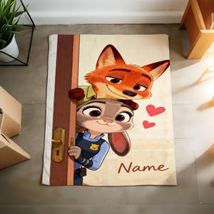 May include: A rectangular beige bath mat featuring cartoon characters Nick Wilde and Judy Hopps from Zootopia. Nick, an orange fox, peeks over a door with Judy, a gray rabbit, in a police uniform. Two red hearts and the word "Name" are also visible.