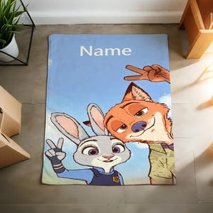 May include: A light blue blanket featuring cartoon characters Judy Hopps and Nick Wilde from Zootopia, with the word "Name" in white. The characters are making peace signs against a sky background.