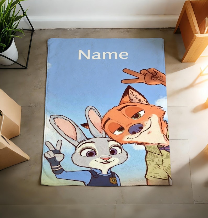 May include: A light blue blanket featuring cartoon characters Judy Hopps and Nick Wilde from Zootopia, with the word "Name" in white. The characters are making peace signs against a sky background.
