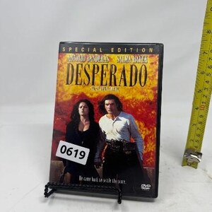 May include: A DVD case for the movie "Desperado" featuring Antonio Banderas and Salma Hayek. The cover has a fiery background with the title in large, bold letters. The DVD is propped up on a black stand with the number "0619" on a white sticker.