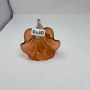 May include: A glass flower with a ruffled, petal-like design in a warm, peachy-orange hue. The stem is clear, and the flower has a label with the number "0330". This decorative piece could be used as a vase or a unique home accent.
