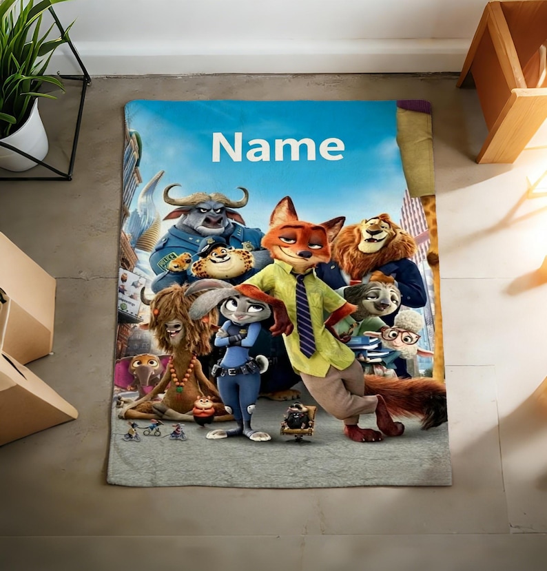 May include: A rectangular blanket featuring characters from the animated film Zootopia. The blanket has a blue sky background with the word "Name" in white. The characters include a fox, a bunny, a lion, and other animals.