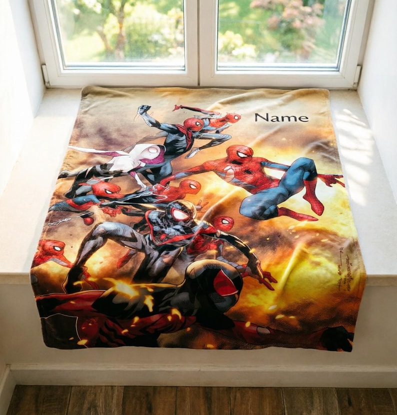 May include: A rectangular fleece blanket featuring a vibrant, multi-character graphic of various Spider-Man figures in dynamic action poses against a fiery orange and yellow background. The word Name is printed in black in the upper right corner.