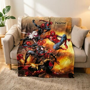 May include: A rectangular fleece blanket featuring a vibrant graphic print of multiple Spider-Man characters in action poses against a fiery orange and yellow background. The word Name is printed in black text in the upper right corner of the blanket.