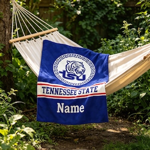 Könnte beinhalten: Ein blaues rechteckiges Handtuch mit dem Logo der Tennessee State University inklusive Tigerkopf, dem weißen Schriftzug TENNESSEE STATE und dem Wort Name in weißen Buchstaben am unteren Rand, drapiert über einer weißen Stoffhängematte.
