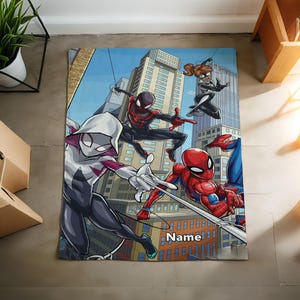 May include: A rectangular blanket featuring a colorful comic book style illustration of four superheroes in action against a city skyline. The design includes characters in red, blue, black, and white suits, with the word Name printed in white text.