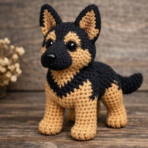 May include: A crocheted German Shepherd dog figurine featuring a black and tan yarn pattern. The plush toy has upright pointed ears, a black nose, and large dark plastic eyes. The body is crafted with a textured stitch pattern throughout.