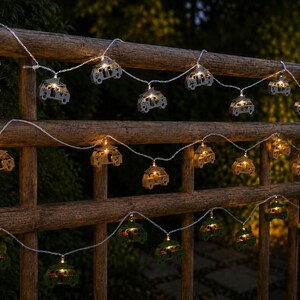 Eine dekorative LED-Lichterkette mit kleinen Van/Kastenwagen-Silhouetten. Die Lichter sind in drei horizontalen Reihen angeordnet und zeigen Van/Kastenwagen in Grau, Beige und Olivgrün, die jeweils von einem warmweißen Licht beleuchtet werden.