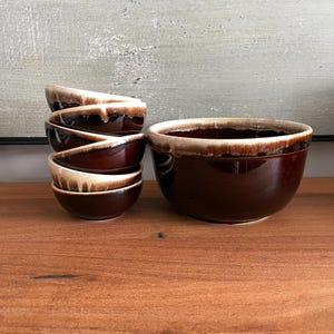 Peut inclure: Ensemble de six bols en céramique marron avec un design bicolore. Les bols ont une finition brillante avec un bord beige clair qui dégouline sur les côtés. Les bols sont empilés à côté d'un plus grand bol assorti.