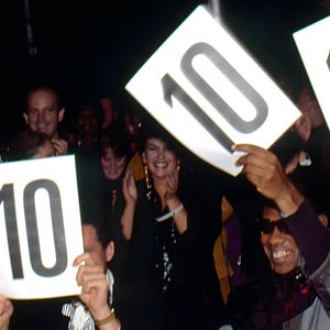 May include: A crowd of people holding up signs with the number 10 on them. The people are smiling and appear to be enjoying themselves. The image is taken in a dimly lit room.