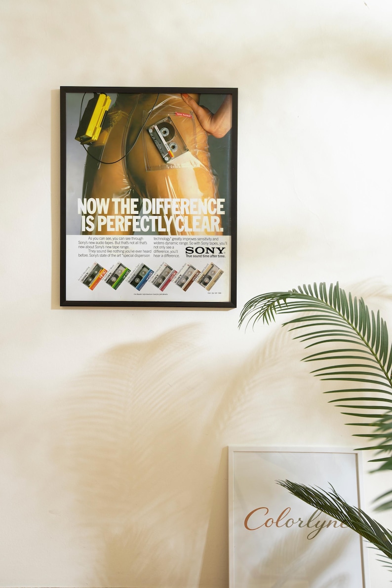 May include: Framed vintage advertisement for Sony audio tapes. The poster features a person in a clear plastic suit with a cassette tape. Text reads "NOW THE DIFFERENCE IS PERFECTLY CLEAR" with the Sony logo and tape examples.