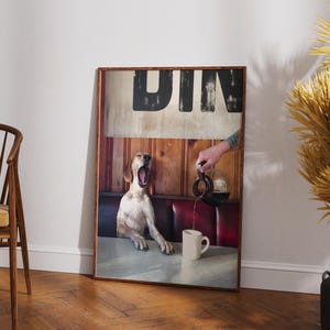 May include: A framed print featuring a dog yawning in a diner setting. The image includes a hand pouring coffee into a mug. The word "DIN" is visible at the top of the print. The dog is white and brown.