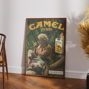 May include: A framed vintage Camel Filters advertisement. The poster features a man smoking, with the brand name in large yellow letters. A pack of cigarettes is also visible. The background has a jungle theme.