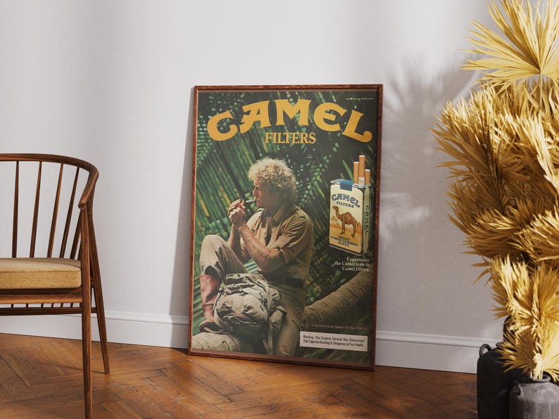 May include: A framed vintage Camel Filters advertisement. The poster features a man smoking, with the brand name in large yellow letters. A pack of cigarettes is also visible. The background has a jungle theme.