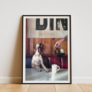 May include: Framed print featuring a dog yawning in a diner booth as coffee is poured into a mug. The word "DIN" is visible above the dog. The scene is set in a diner with red booth seating and wooden paneling.