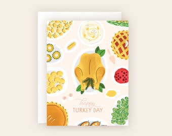 May include: A pink card with a hand-drawn illustration of a Thanksgiving dinner spread. The illustration includes a roasted turkey, mashed potatoes, green beans, cranberry sauce, and pumpkin pie. The text "happy TURKEY DAY" is written in cursive on the card.