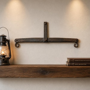 May include: A dark brown wooden floating shelf holding a black metal lantern with a lit flame, a dark iron wall-mounted bracket with two hooks, and two stacked books titled American Farm Implements and Rural Architecture on a light wall.