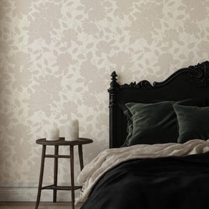 May include: A bedroom scene featuring a black bed frame with dark green pillows and a black comforter. The wall is covered in a floral wallpaper pattern in a neutral color. A small wooden side table holds two white candles.