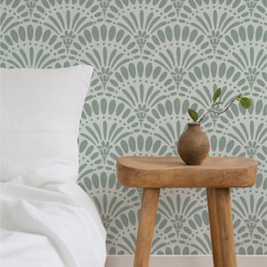 May include: A bedroom scene featuring a white pillow and bedding against a patterned wall. The wall has a repeating fan-like design in a muted green color. A small, wooden stool holds a brown vase with a sprig of greenery.