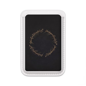 May include: A rectangular black phone case with a white border. The case features a gold-colored inscription in a circular pattern. The design is set against a dark background, creating a striking contrast.