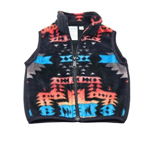 May include: A black fleece vest with a colorful geometric pattern in shades of red, orange, blue, and white. The vest has a zipper closure.