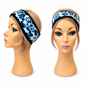 May include: A fleece headband featuring a blue and white leopard print pattern with black trim. The headband is shown from both a side profile and a front-facing view on a mannequin head, displaying the soft texture and the bold animal print design.