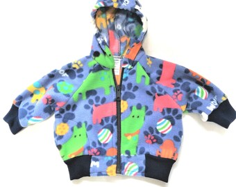 May include: A blue fleece jacket with a hood, featuring a colorful print of dogs, paw prints, and balls. The jacket has a zipper closure and a navy blue ribbed waistband.