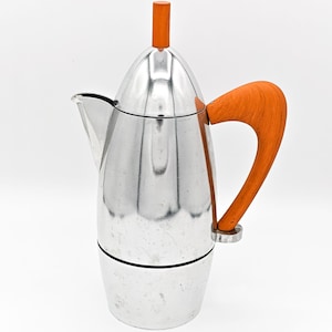 Op de afbeelding: Een gepolijste zilverkleurige metalen koffiepot met een hoog, taps toelopend lichaam en een puntig deksel. De pot is voorzien van een gebogen, lichtoranje houten handvat en een bijpassende kleine houten knop op het deksel, met een schenktuit.