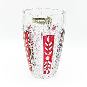 May include: A clear and ruby red cut lead crystal vase featuring intricate geometric starburst patterns and vertical panels with etched leaf motifs. A gold and black sticker near the rim reads BOHEMIA CZECHOSLOVAKIA 24% PbO.