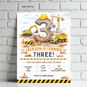 Pode incluir: Um convite de aniversário com tema de construção. O design apresenta um grande número 3 de pedra, um capacete amarelo e veículos de construção. O texto diz "Jackson está fazendo TRÊS!" e detalhes do evento.